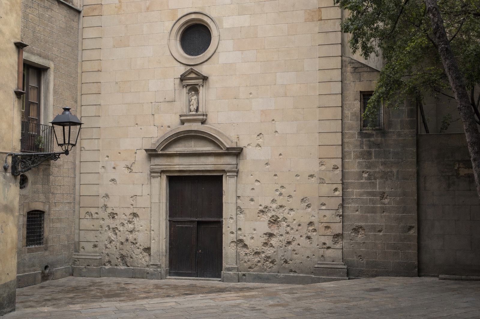 The church façade at Plaça de Sant Felip Neri carries the scars of the 30 January 1938 bombing