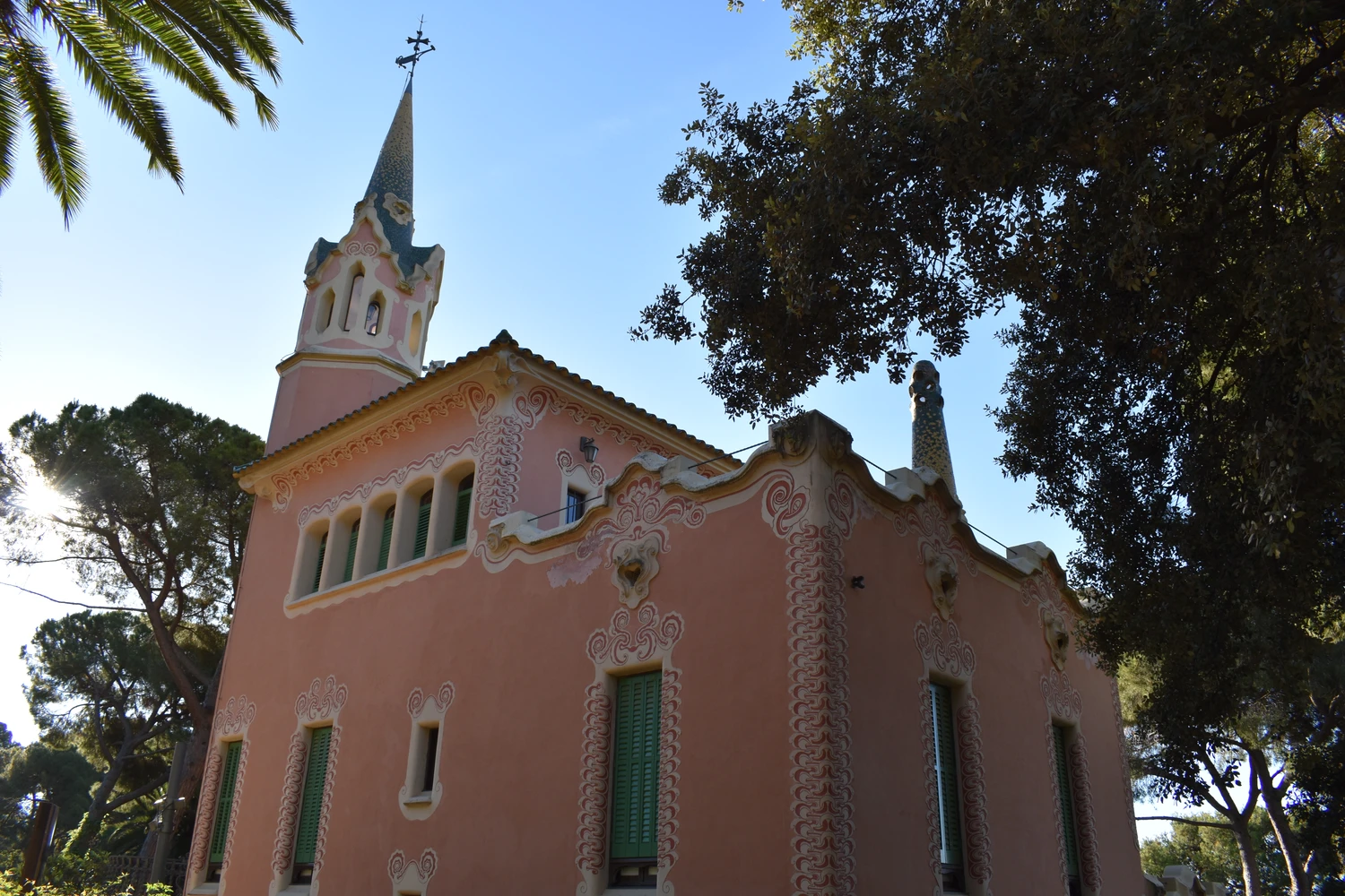 The pink exterior and decorated tower of the Gaudí House Museum among the park’s trees
