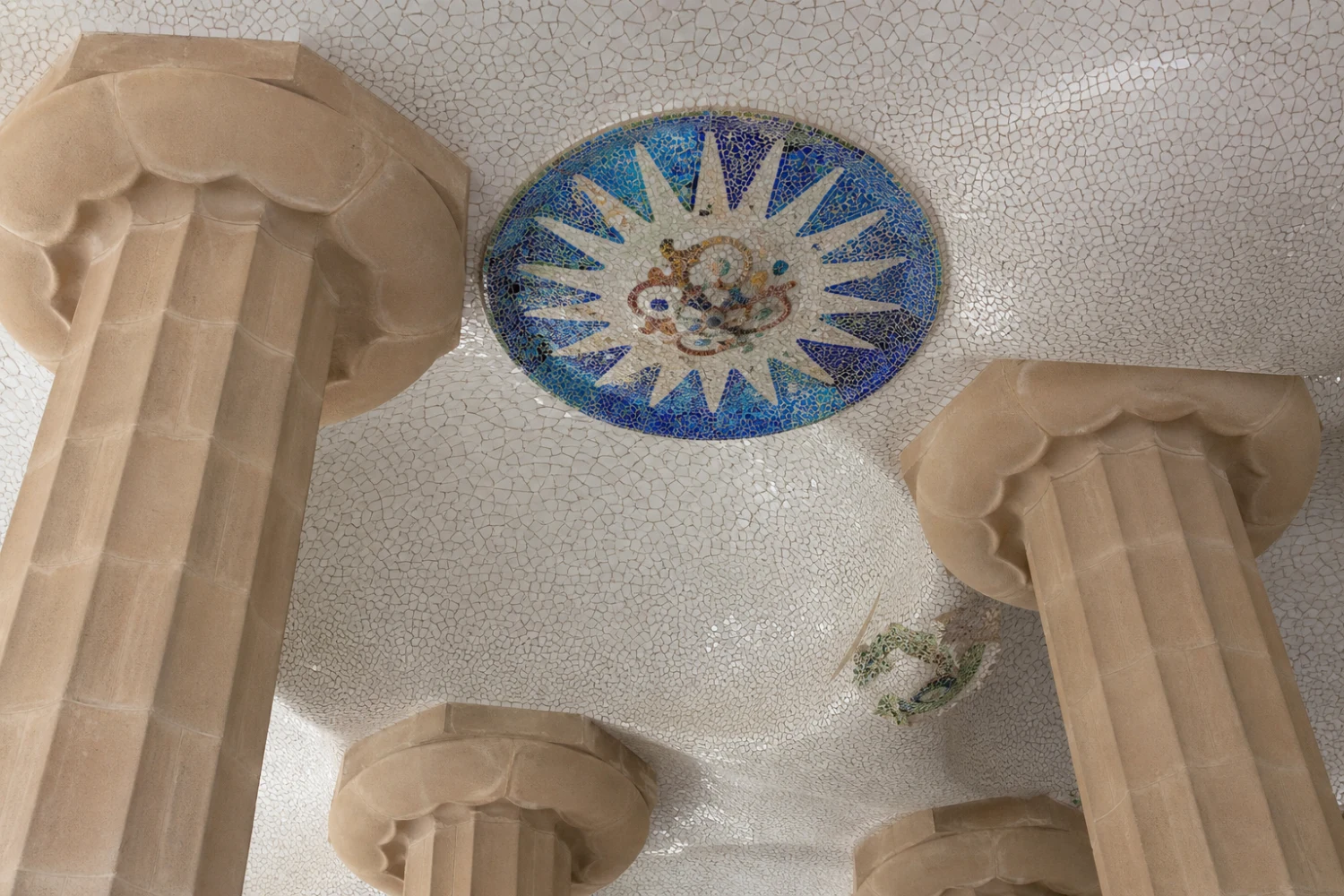 A place-led close view isolates the white tile-shard domes and a Jujol medallion above the column capitals