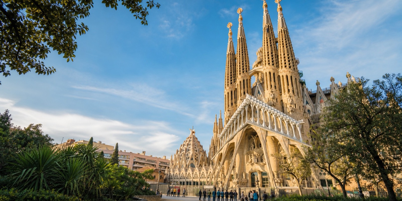 The Sagrada Família rises beyond trees and garden planting in Barcelona