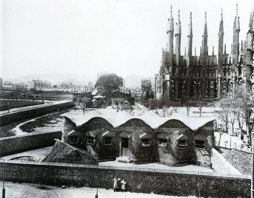 The Sagrada Família Schools stand in snow in an archival view, with construction rising behind