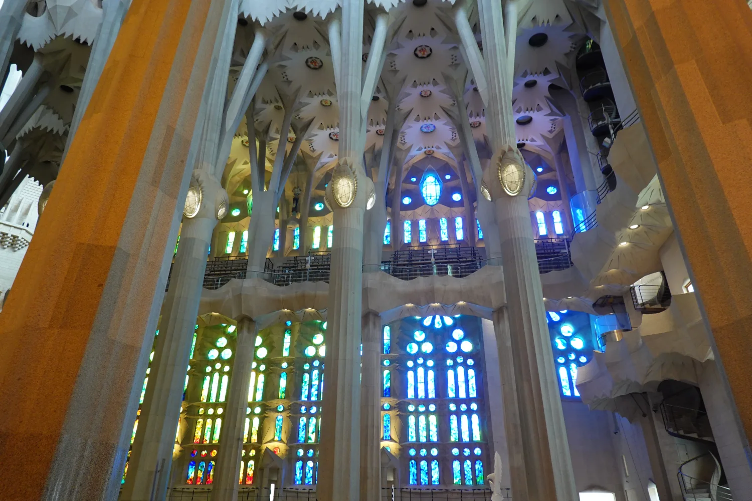 Blue and green stained glass washes branching columns on the Nativity side of the nave