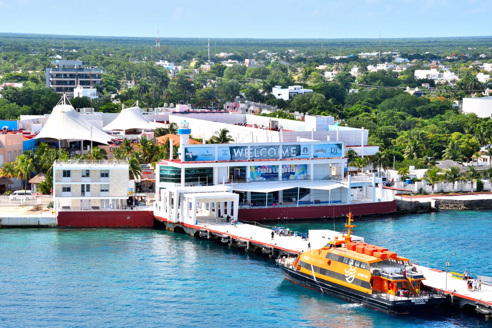 Punta Langosta's waterfront joins a passenger vessel, terminal infrastructure, commercial space and the neighbourhoods of San Miguel.