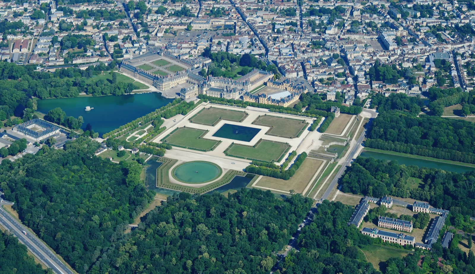 An aerial view of Fontainebleau shows multiple courts and wings between the town, gardens, water and forest.