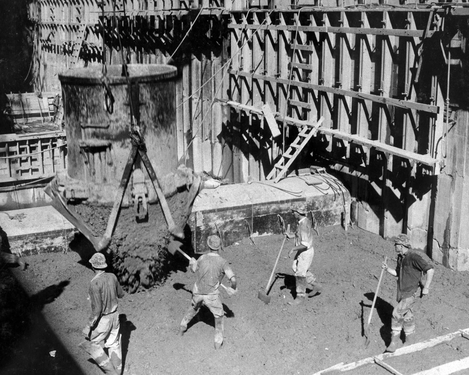 Workers spread newly discharged concrete beneath a suspended bucket at Hoover Dam in September 1933