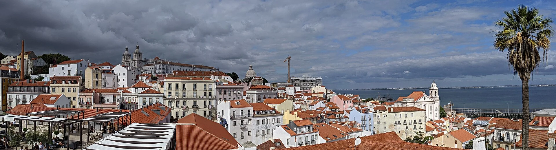 A broad view from Portas do Sol shows Alfama descending through churches and roofs toward the Tagus estuary.