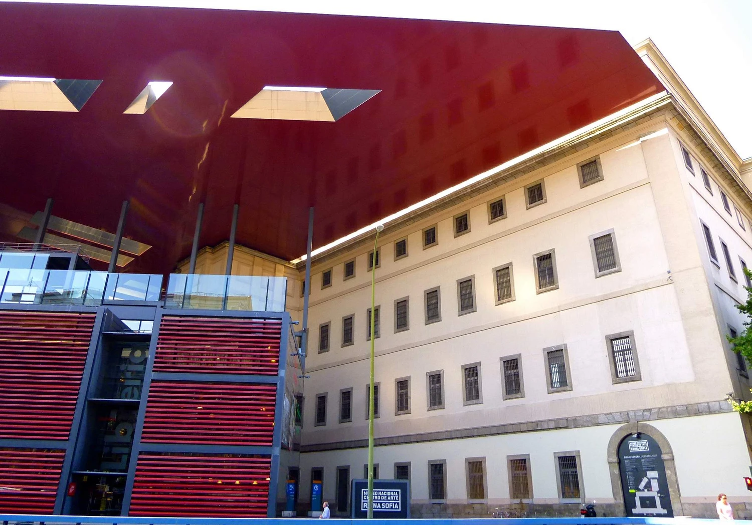 Nouvel’s projecting red roof and glass connection stand beside the pale masonry and barred windows of the former hospital.