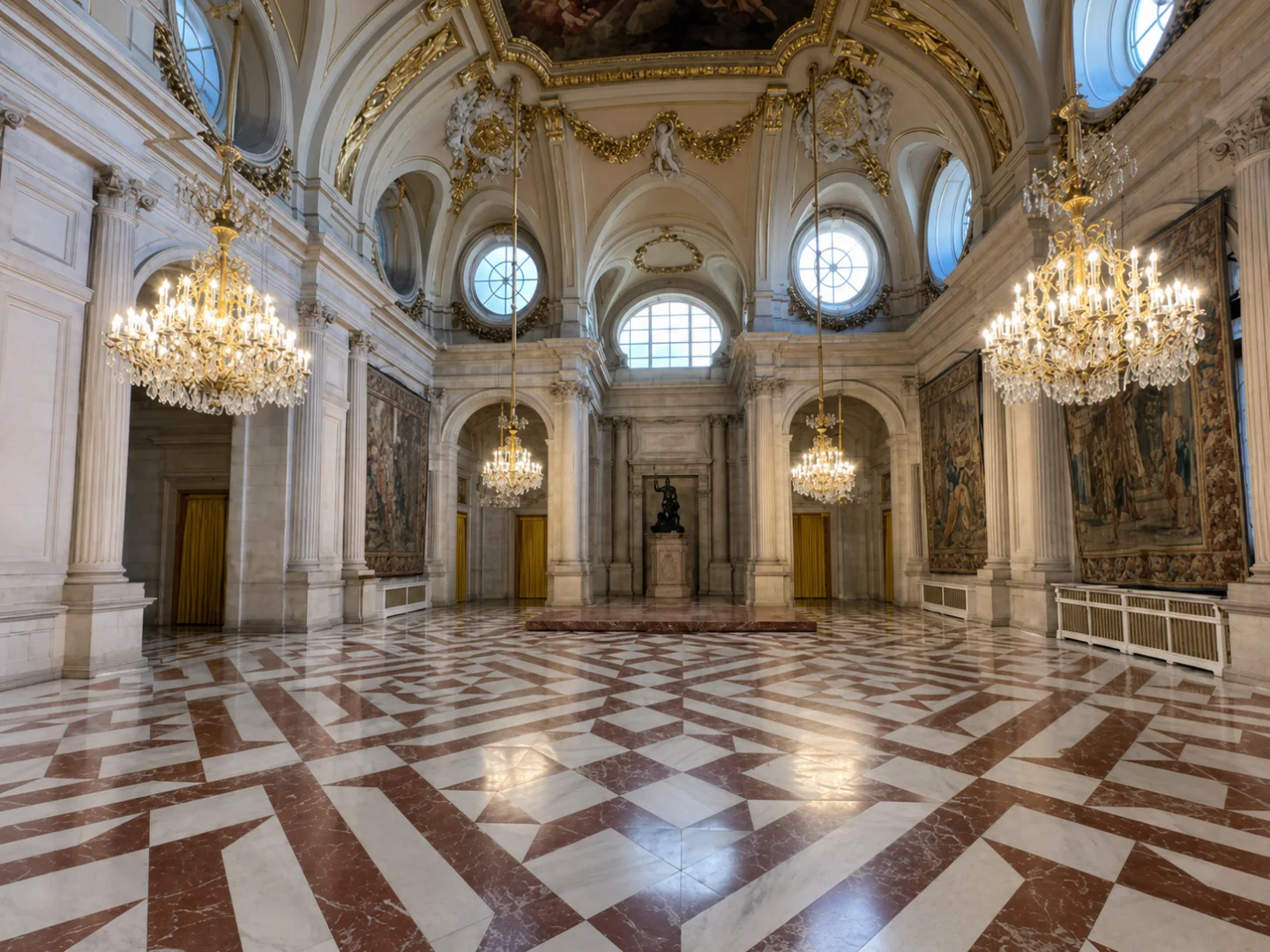 An empty ceremonial gallery with marble floor, tapestries, chandeliers and tall windows recedes through the palace.