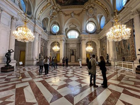 Visitors crossing a marble and tapestry-lined gallery inside Madrid’s Royal Palace
