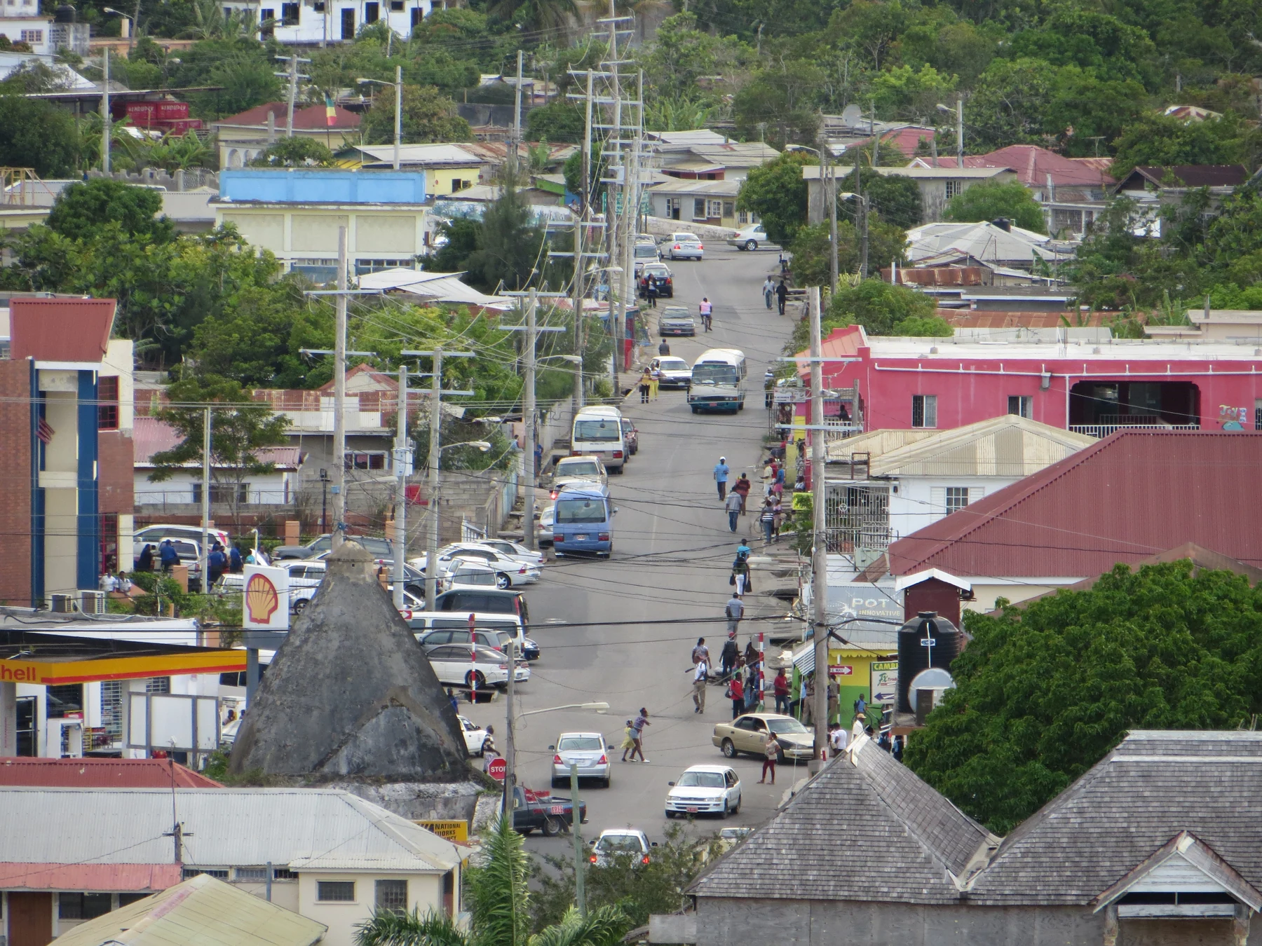 An elevated view along a busy Falmouth street, with low buildings, vehicles and hills beyond.