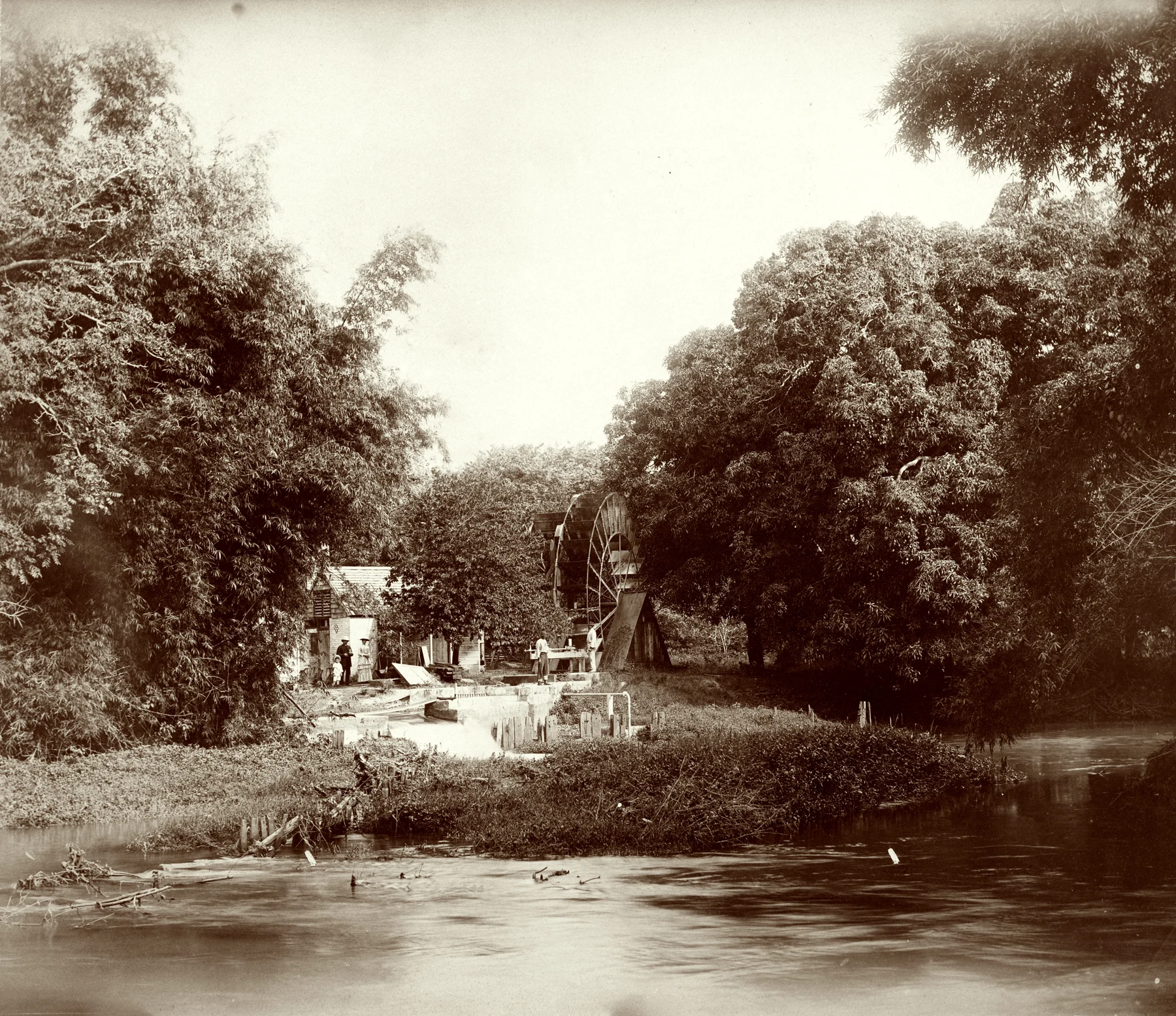 A historic photograph of the Martha Brae waterwheel beside the river, with people and trees showing its scale.