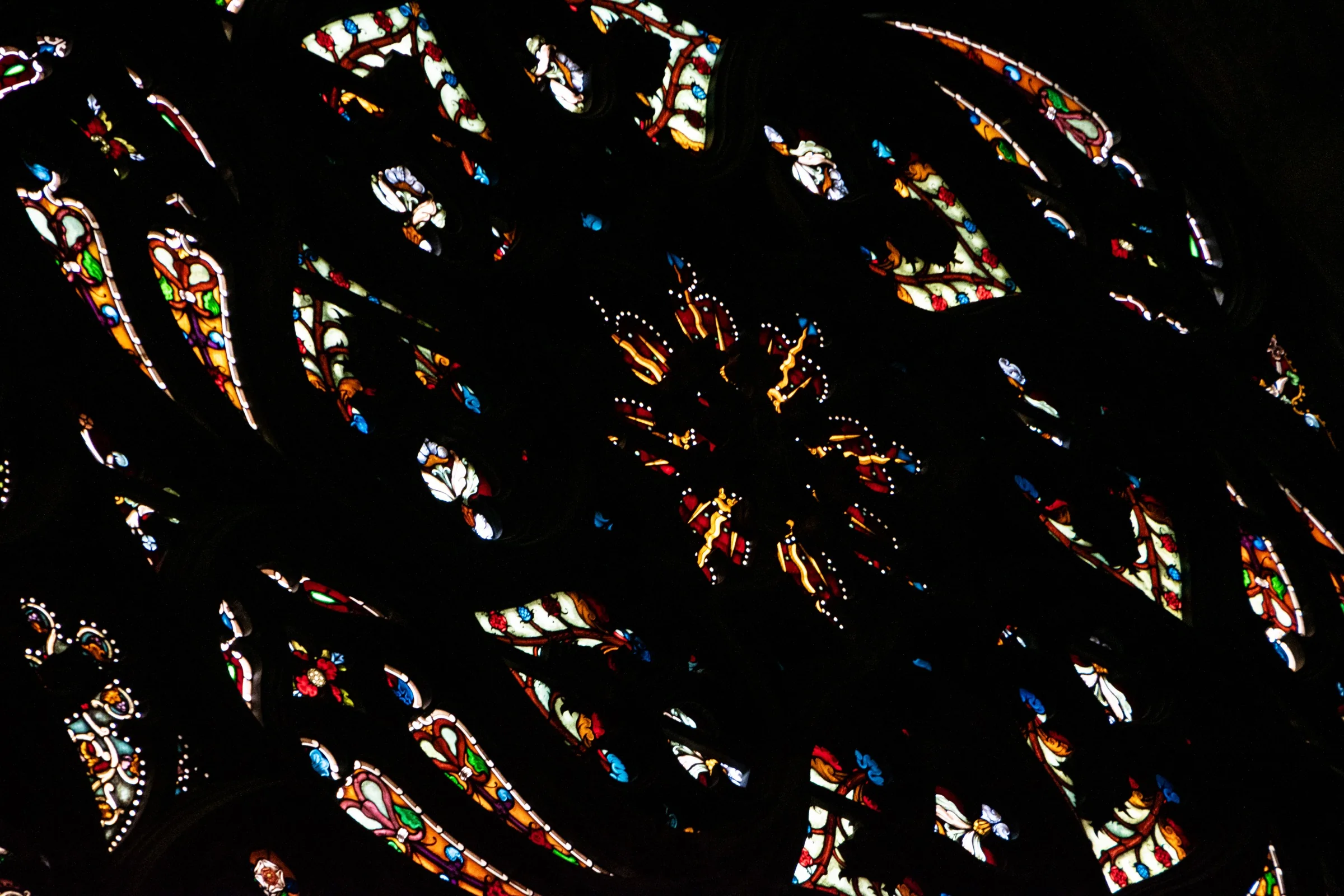 A close view of Milan Cathedral stained glass, with small coloured narrative fragments held within dark stone and lead divisions
