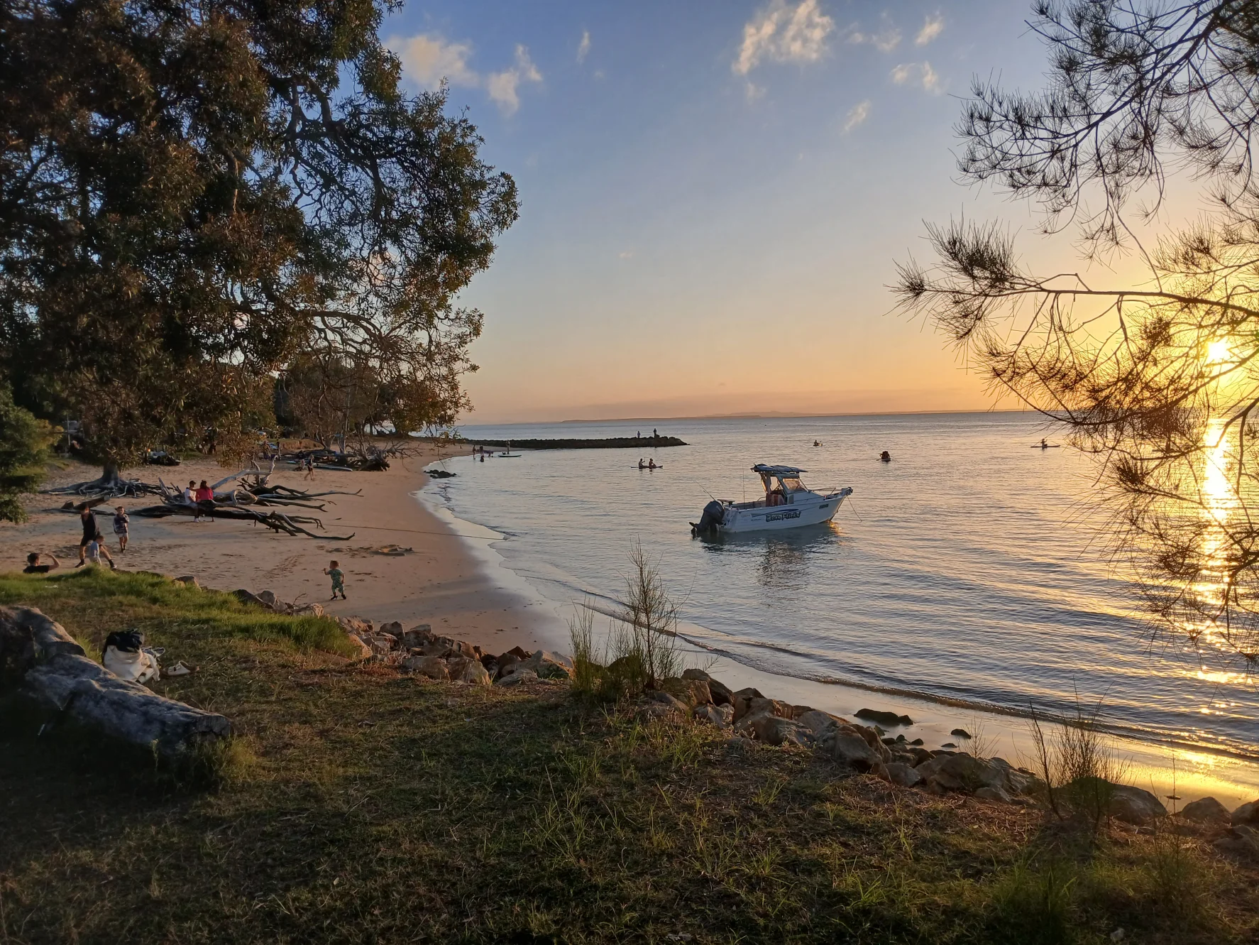 People and a small boat share the foreshore at Amity Point as evening colour spreads across Moreton Bay.