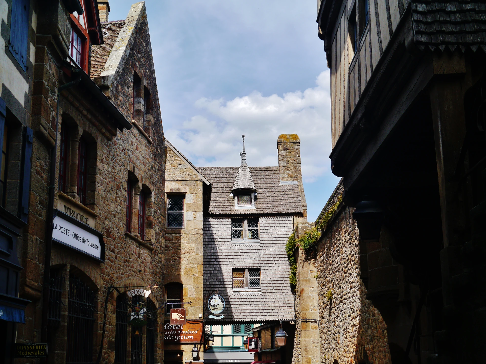 Stone and timber buildings crowd the narrow Grande Rue, with signs for village services and accommodation below the rooflines.