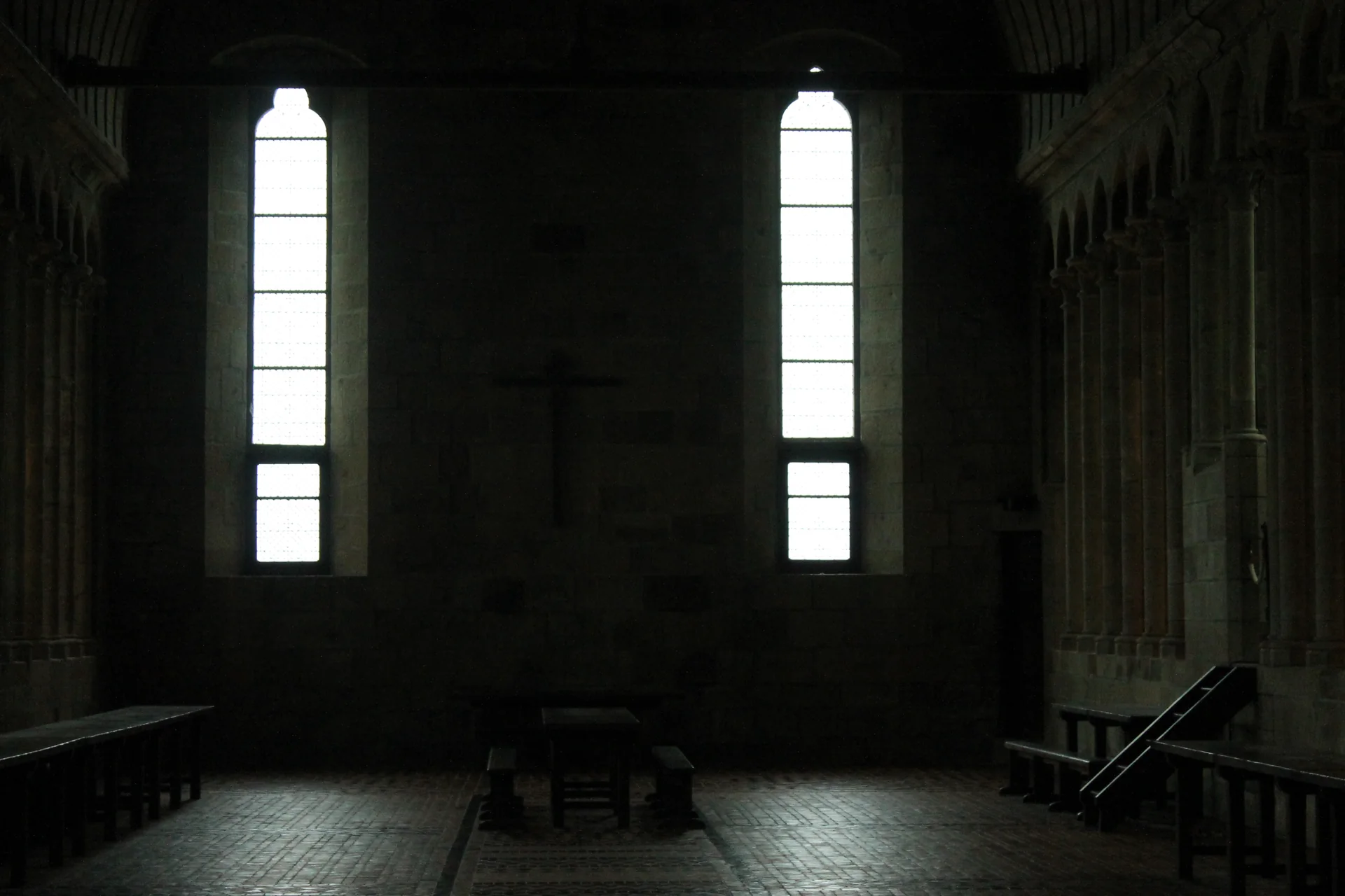 The abbey refectory is seen as a long, dark stone hall, with tall narrow windows admitting controlled vertical shafts of light.