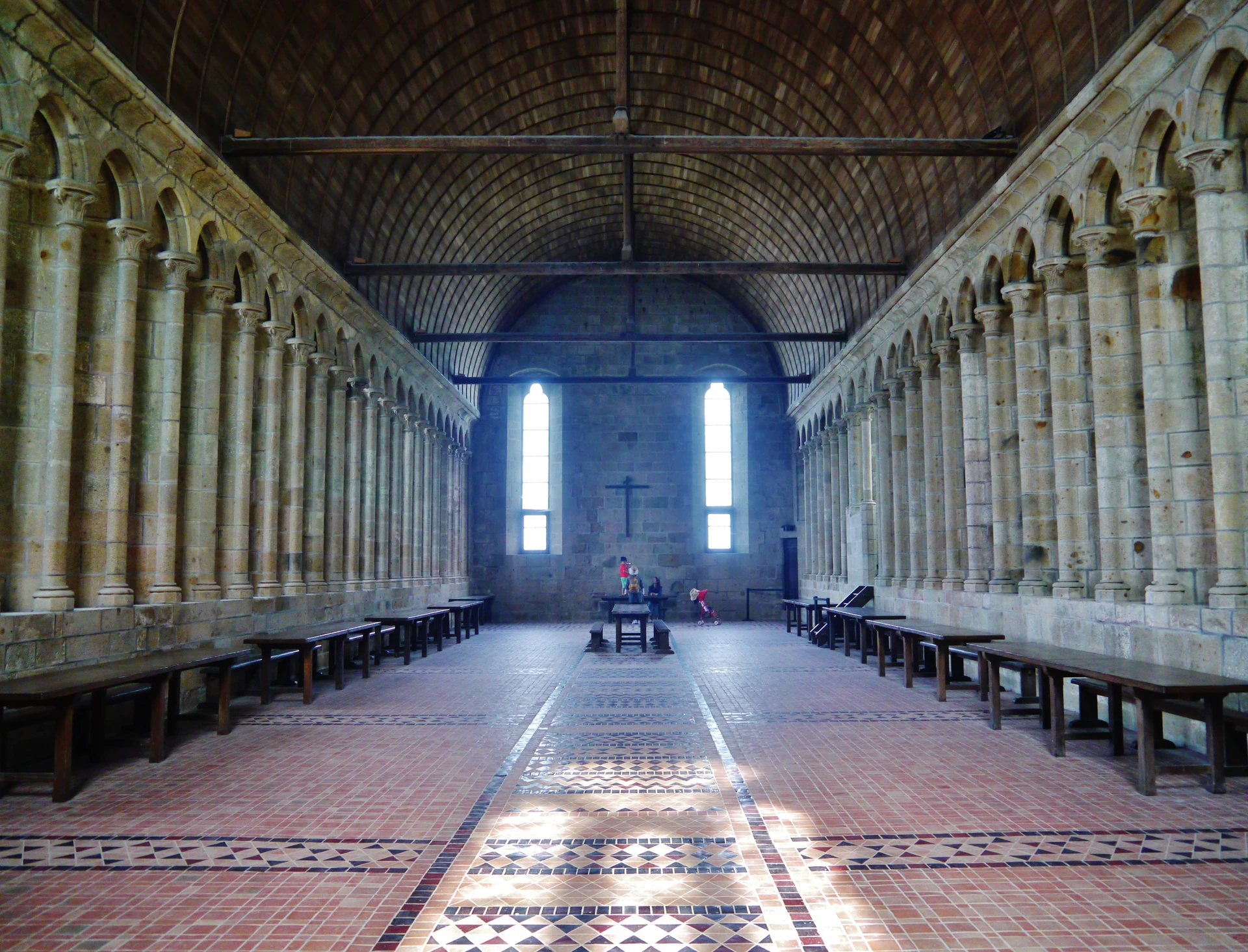 The long abbey refectory has a timber ceiling, closely spaced stone window reveals and rows of tables beneath its high walls.