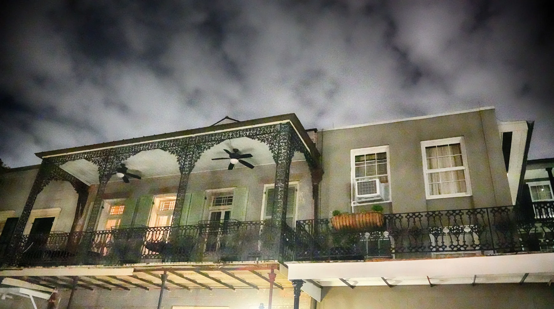 A night view looks up at galleries, shutters, fans and air-conditioning units beneath a stormy sky