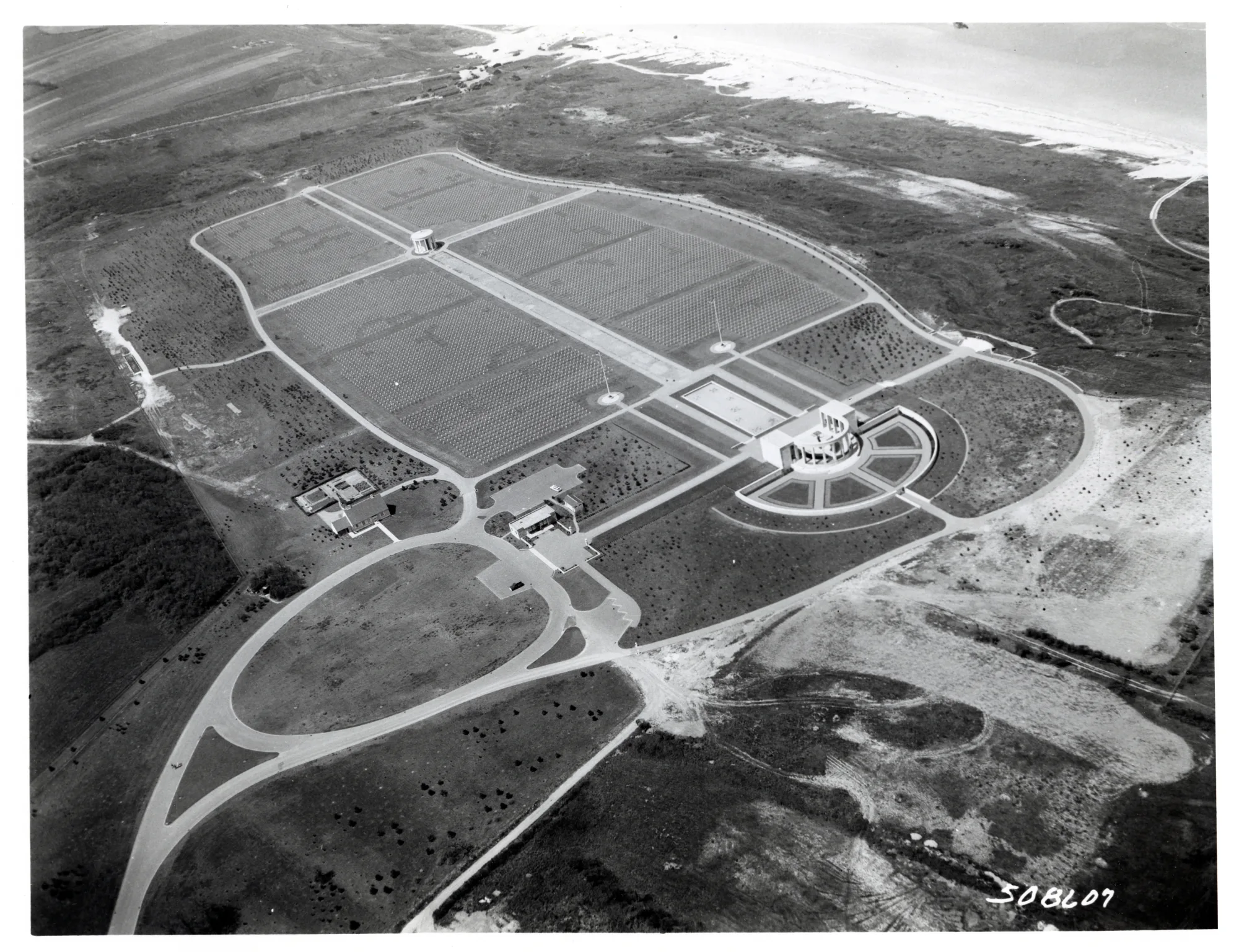 Aerial view of Normandy American Cemetery showing the formal burial fields, memorial axis and coastline