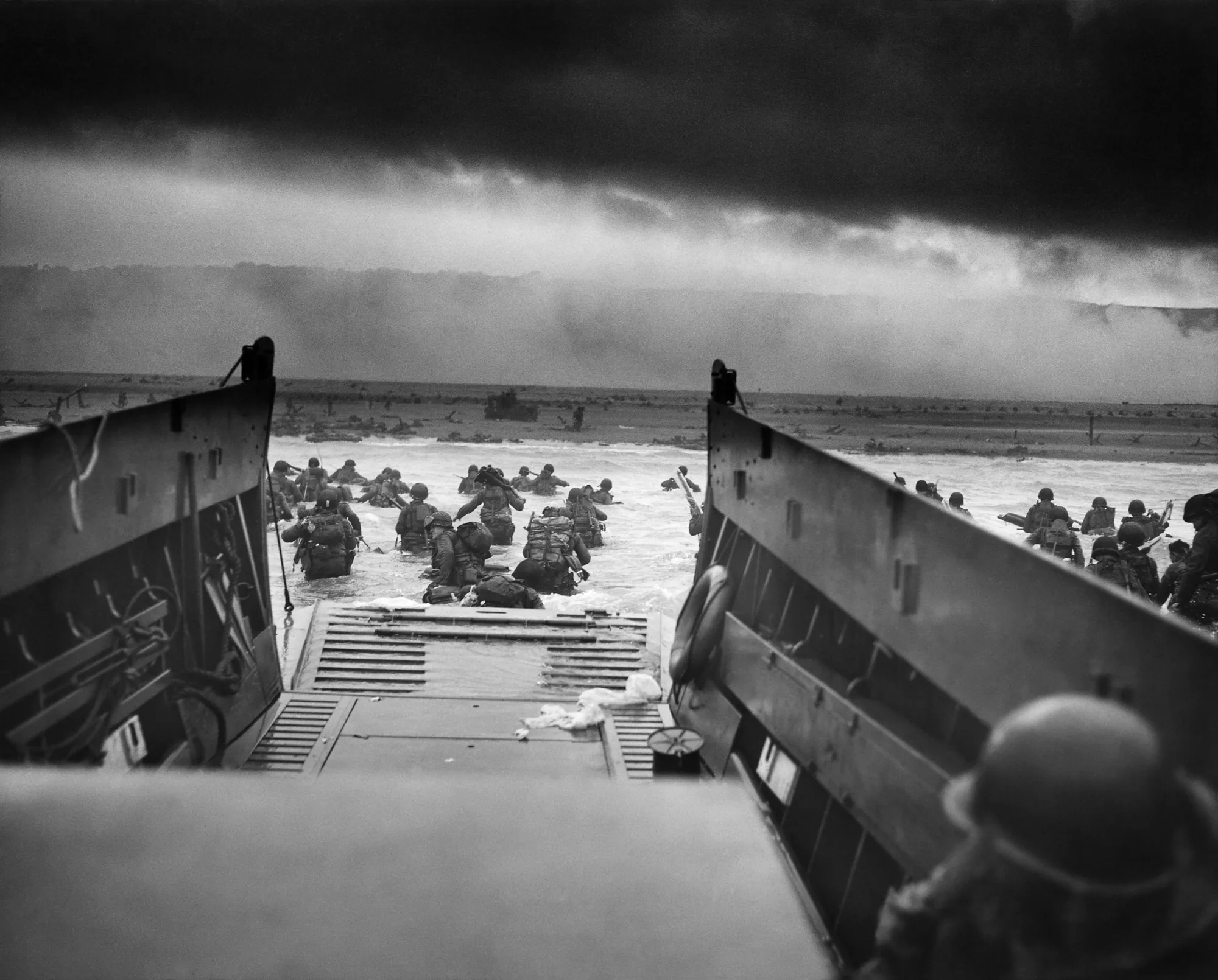 U.S. troops leave a Coast Guard-manned landing craft and move through water toward Omaha Beach on 6 June 1944
