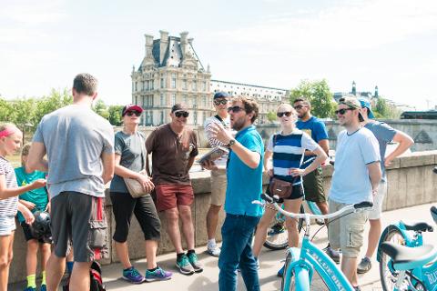 A guide speaks to a small bicycle group at a Louvre-side stop.
