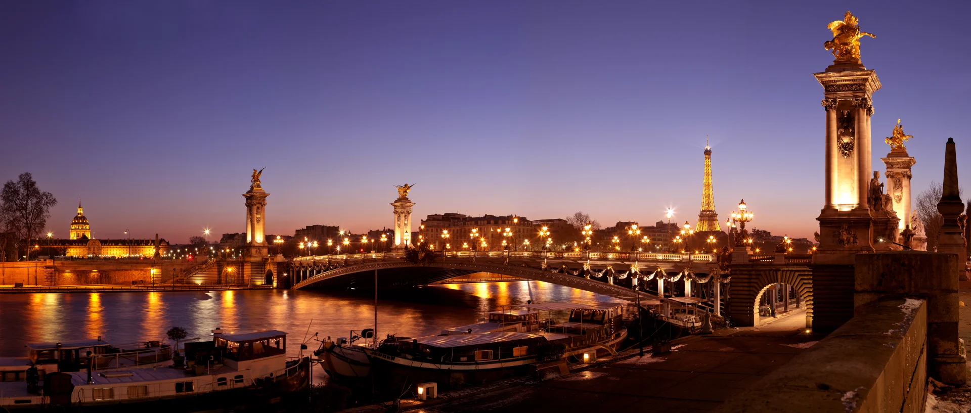 Pont Alexandre III crossing the Seine at dusk with the Invalides dome and Eiffel Tower beyond.