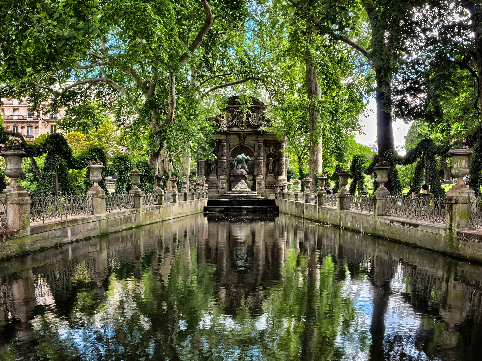 The Médicis Fountain terminates a long shaded basin beneath mature trees in the Luxembourg Garden.