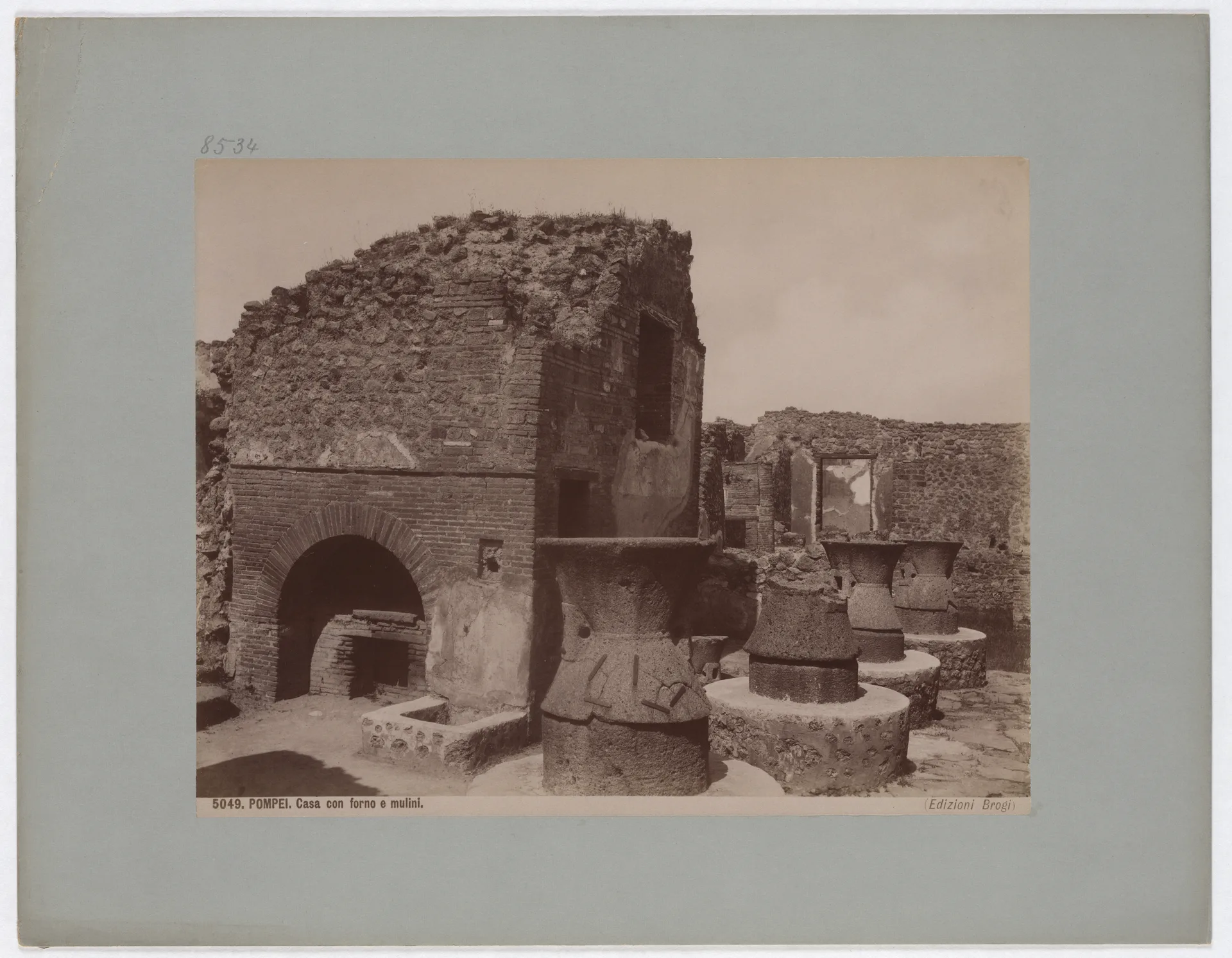 A nineteenth-century archival photograph shows Pompeii lava millstones and a brick oven in an excavated bakery