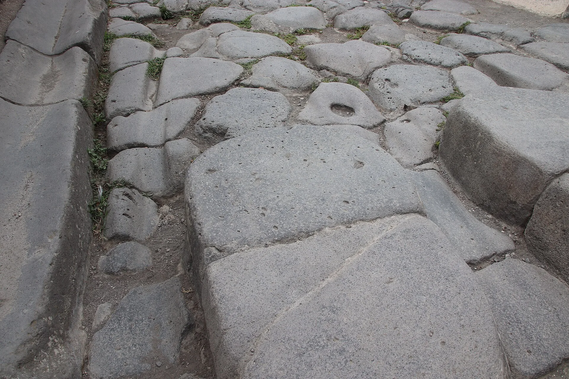 Close view of a raised crossing stone, volcanic paving and a wheel rut in a Pompeii street
