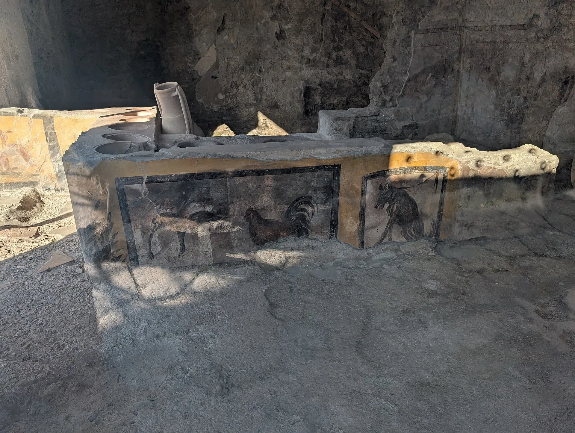 A decorated Pompeii food counter has round storage openings and painted panels showing animals