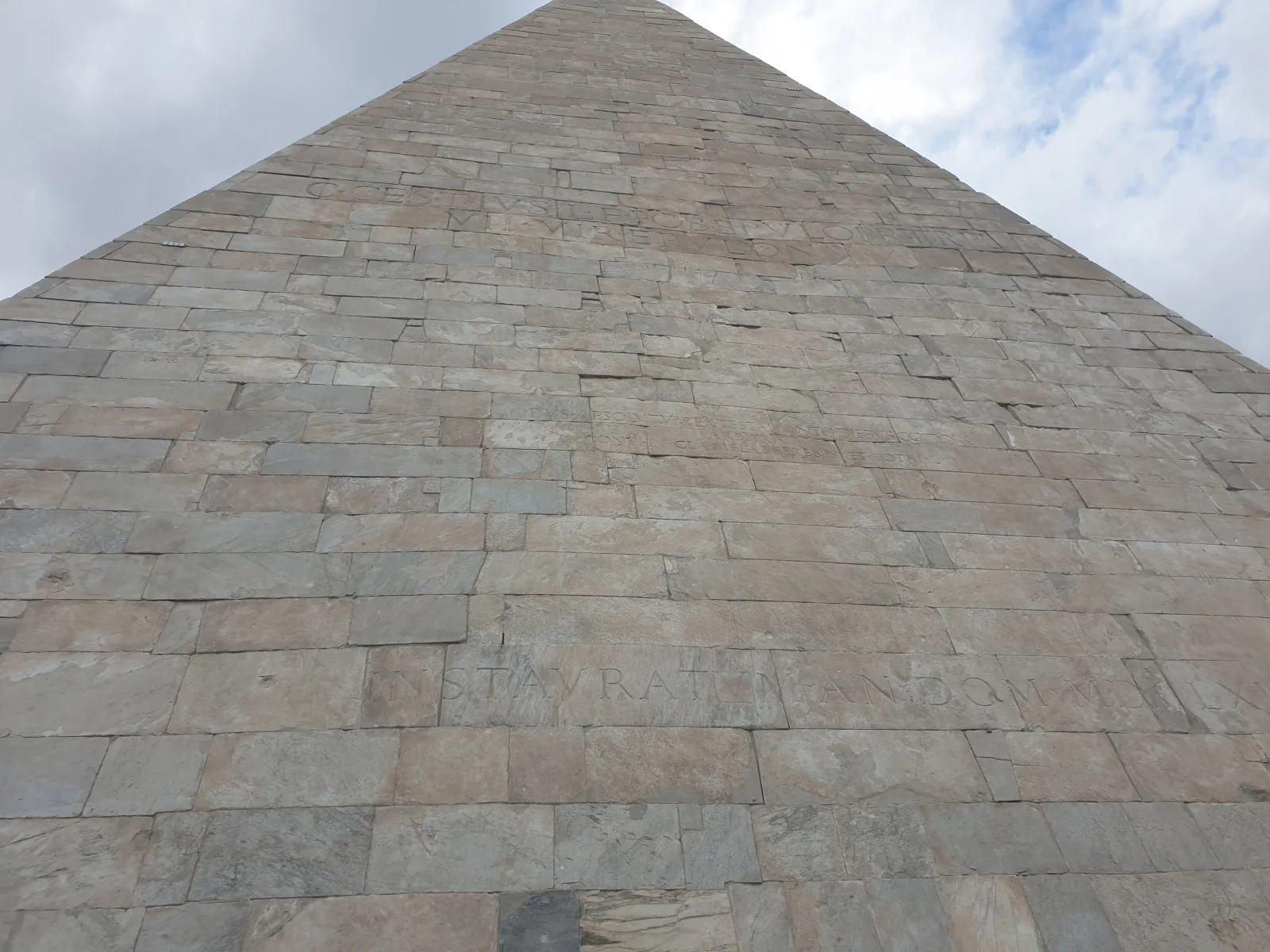 The marble-clad east face of the Pyramid of Cestius rises above its Latin inscriptions.