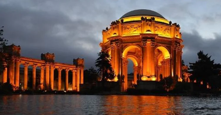 The Palace of Fine Arts rotunda glows beside its lagoon beneath a darkening sky