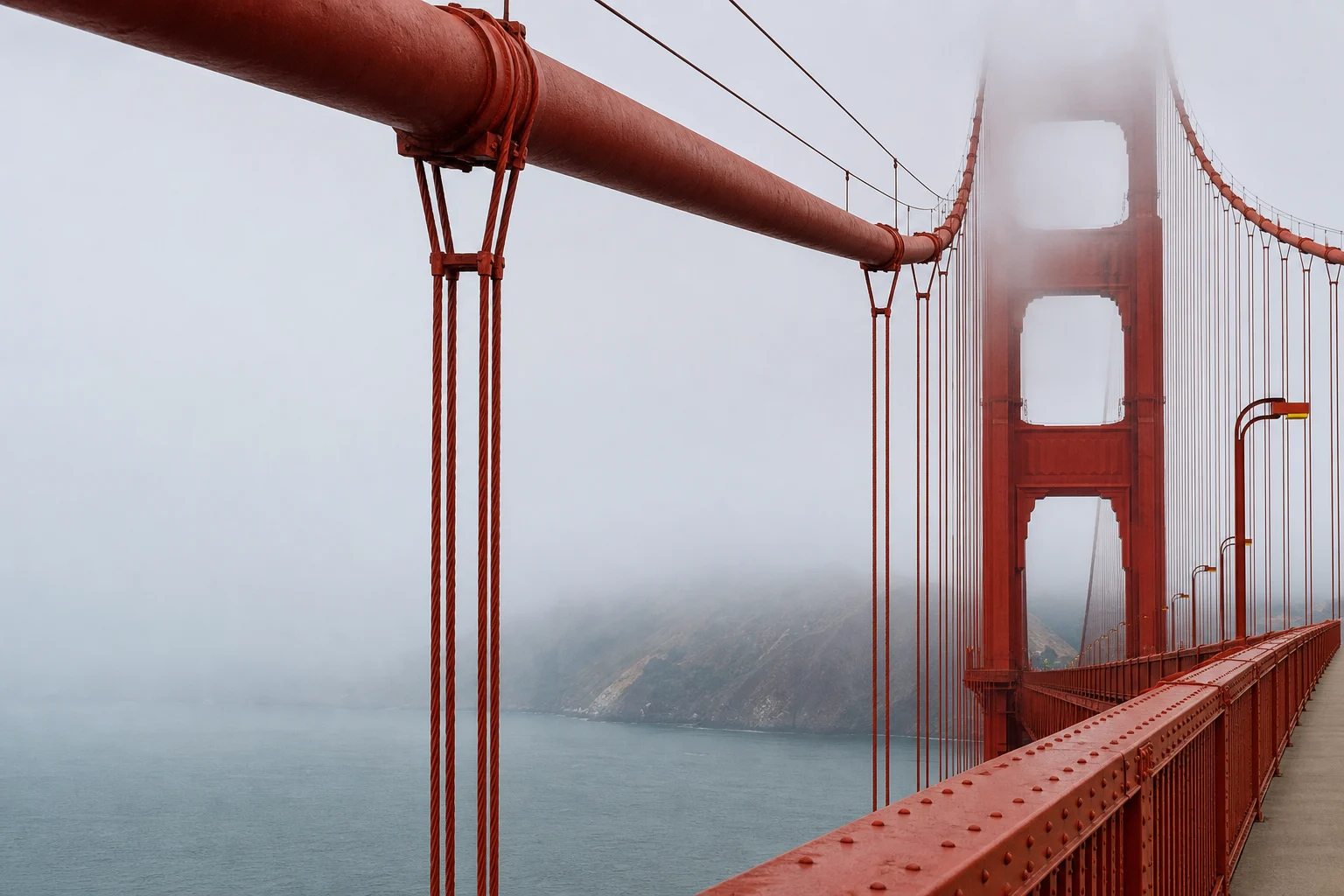 A close architectural view of the Golden Gate tower, main cable and suspenders in fog