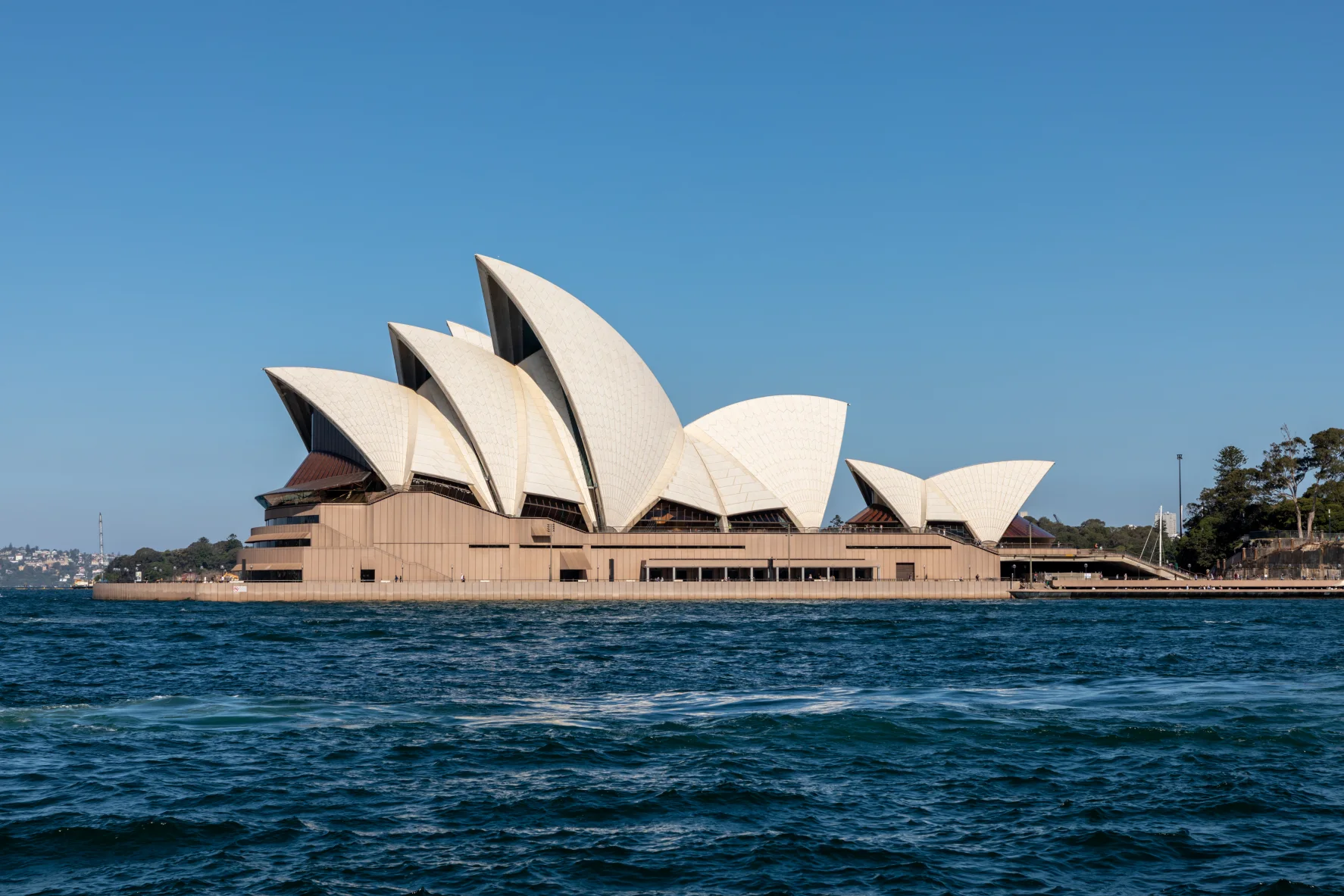 The Sydney Opera House viewed across the harbour, with its interlocking shell roofs legible above the broad podium.
