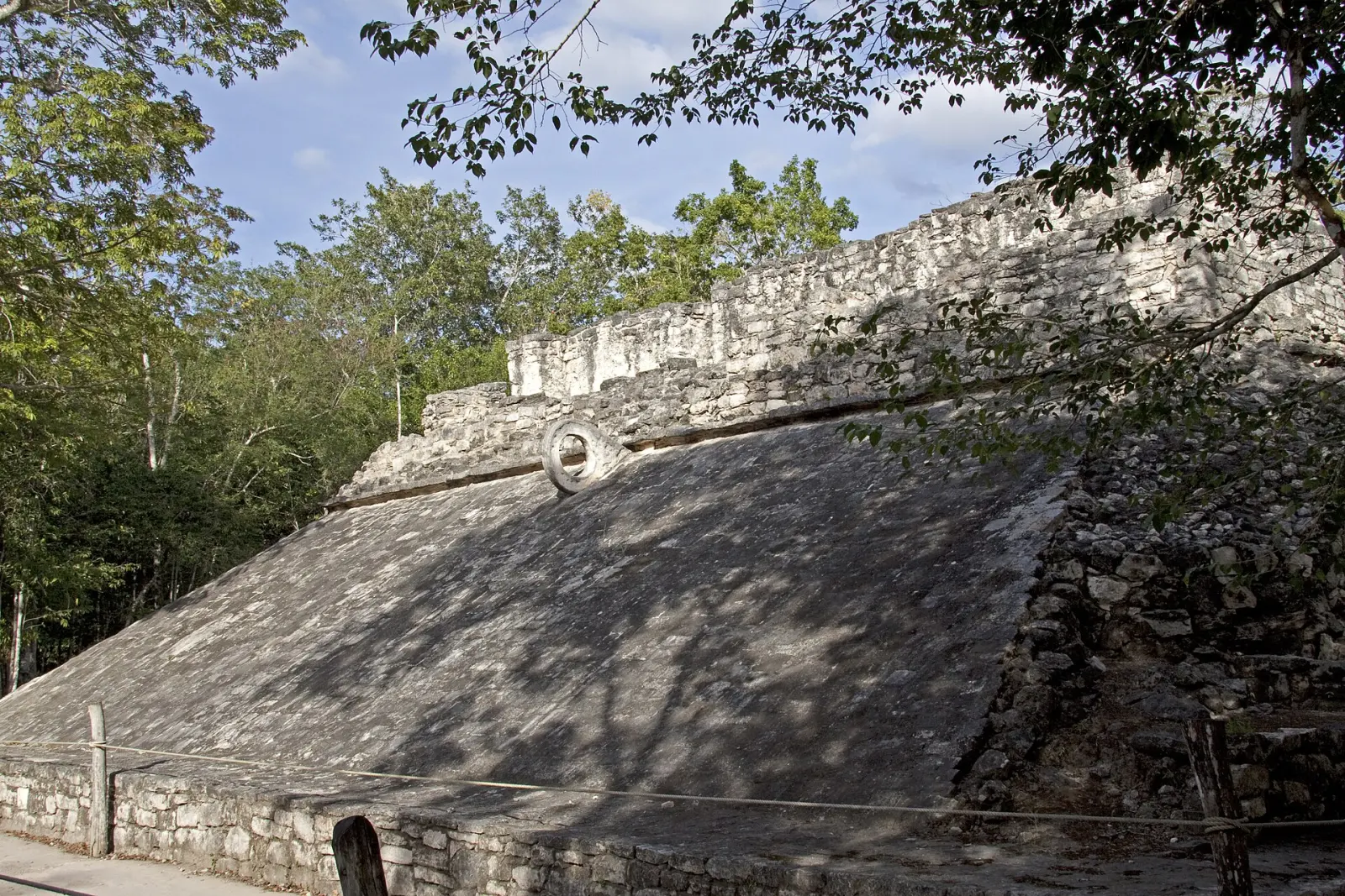 A sloping wall and stone ring define one ball court at Cobá.