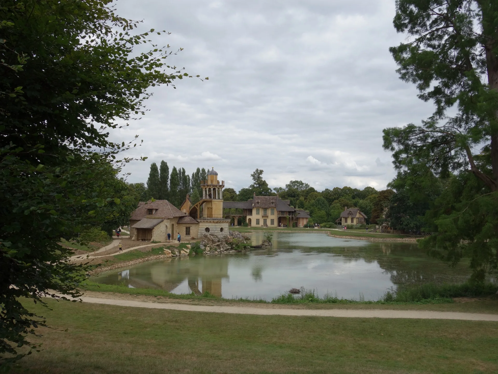 The Queen’s Hamlet seen across its lake, with the Marlborough Tower and rustic buildings embedded in a composed landscape.