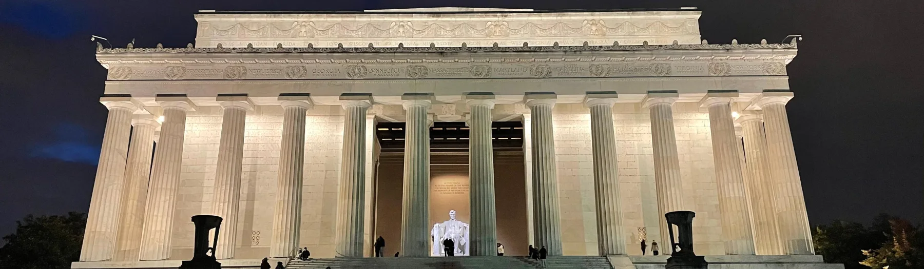The illuminated Lincoln Memorial exterior at night with the seated statue visible between columns.