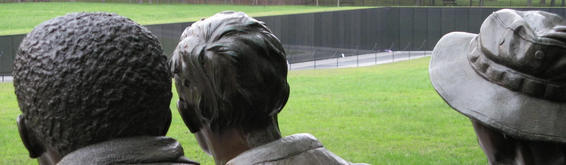The Three Servicemen figures seen toward the descending polished wall of the Vietnam Veterans Memorial.